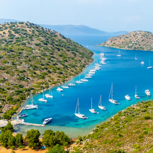 Marmaris körfezinde, turkuaz bir koyda demirlemiş yat filosunun havadan görünümü.