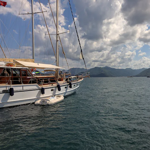 Marmaris'te sakin suda duran ahşap bir gulet ve arkasında kıyı dağları.